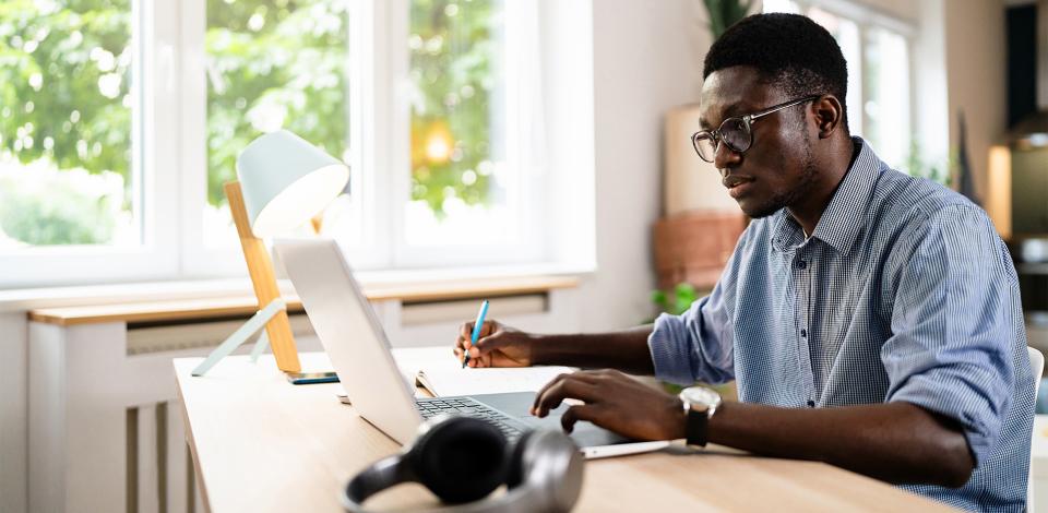 A young African-American man working on a laptop in a home office space.