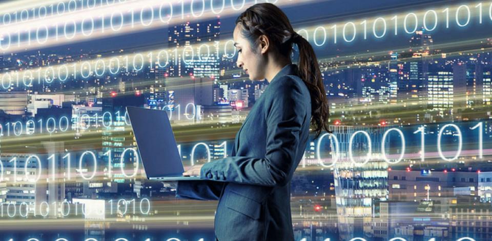 Woman standing in front of backdrop of code holding a laptop