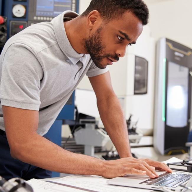 Male engineer using CAD programming software on laptop.